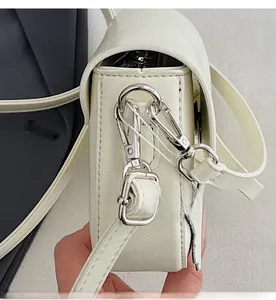 Detail showing the detachable silver hardware hooks on a white faux leather crossbody bag