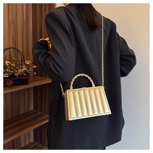 Detail of gold box clutch featuring vertical ribbed texture and knot handle on a model