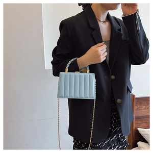 Detail of light blue box handbag featuring vertical quilted texture and gold chain strap
