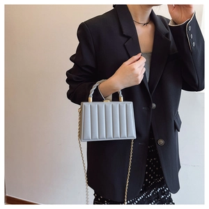 Detail of grey pleated box bag with twisted handle and golden chain on a fashion model