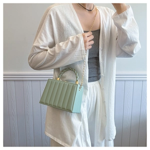 Detail of light green square bag with vertical texture and woven handle on a model