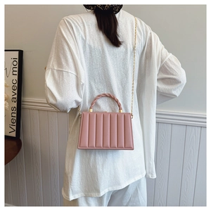 Detail of pink pleated handbag with twisted handle and gold chain on model in French room