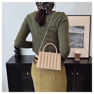 Detailed back view of a beige vertical quilted handbag with a twisted handle and gold chain