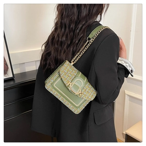 Détail du sac bandoulière en tweed vert avec boucle en U dorée porté sur un blazer noir