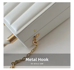 Detail of light gold hardware hooks and chain on a white wavy texture handbag