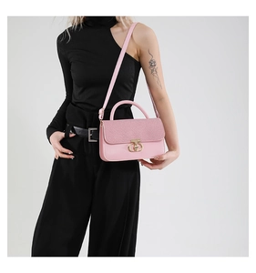 Detail of pink handbag with textured flap and gold circular lock shown on a model