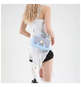 Detail of light blue crossbody bag with textured grey flap and golden metal lock