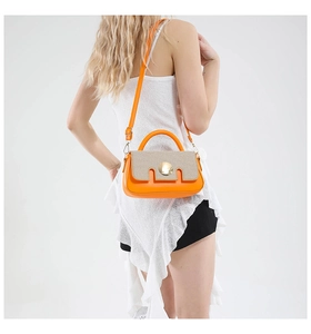 Detail of orange and beige crossbody bag featuring woven texture and gold round buckle
