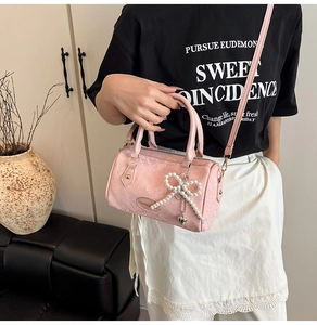 Detail of pink embossed leather pillow bag with pearl bow pendant and crossbody strap