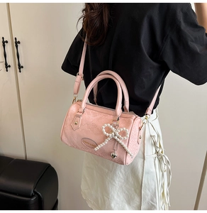 Pink boston bag with snake pattern texture featuring pearl bow charm and shoulder strap