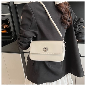 Detail of a creamy white rectangular shoulder bag with a silver twist lock on a model