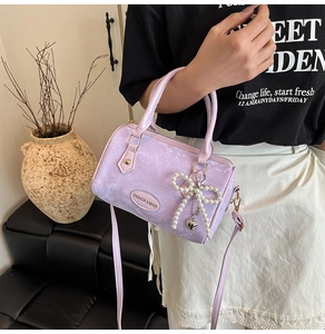 Close-up of lavender snakeskin Boston bag with pearl bow charm and metal logo tag