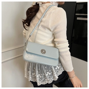 Side view of light blue glossy leather shoulder bag with silver turn-lock on a model