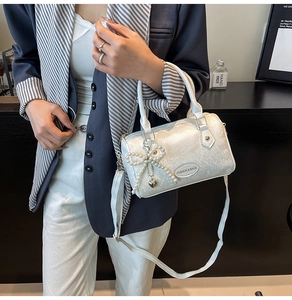 Detail of white embossed Boston bag with pearl bow charm and heart metal pendant