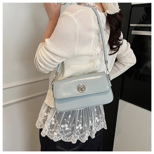 Detail of light blue patent leather shoulder bag with silver circular twist lock on model