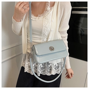 Close-up of a light blue glossy crossbody bag with a round silver clasp on a model