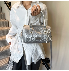 Detail of silver snakeskin texture bag with pearl bow charm and metal hardware accents
