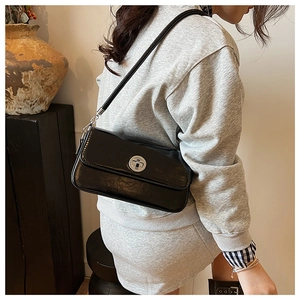 Detail of black glossy leather underarm bag featuring a silver metal circular twist lock