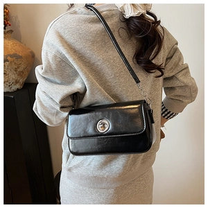 Side view of elegant black glossy shoulder bag with silver clasp on female model