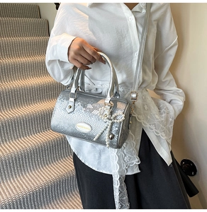 Detail of silver snakeskin Boston bag featuring pearl bow charm and metal logo tag