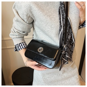 Detail view of black rectangular crossbody bag with silver twist lock and paisley scarf accessory