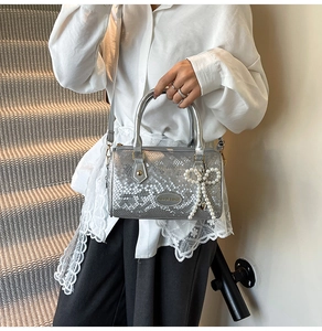 Detail showing silver snake texture cylinder bag with pearl bow charm and brand plaque