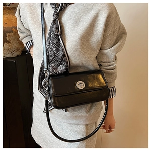 Side view of black glossy leather square crossbody bag with silver round twist lock on model