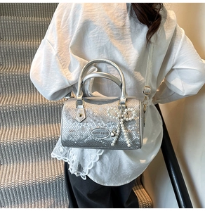 Detail of silver pillow bag with snake pattern embossing and pearl bow charm accessory