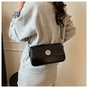 Detail of minimalist black patent leather shoulder bag with silver twist lock on a model