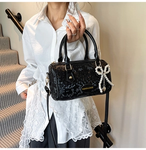 Detail of black snake-patterned cylinder bag with a pearl bow charm and logo detail