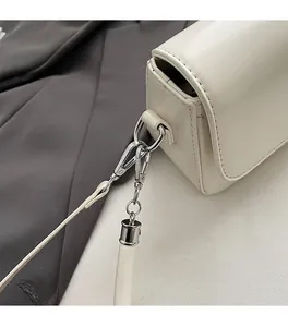 Close-up of silver metal hardware and lobster clasp on white leather crossbody bag