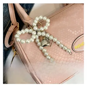 Detail of pearl bow charm and metal heart tag on a pink snakeskin leather handbag