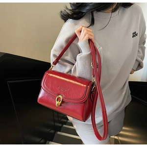 Détail du sac bandoulière rouge avec boucle dorée à double anneau sur fond gris
