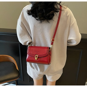 Détail du mini sac carré en cuir rouge brillant avec boucles dorées porté sur gris