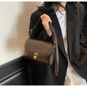 Gros plan du sac bandoulière en cuir marron brillant avec boucle dorée torsadée