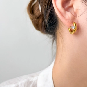 Close-up of a 18K gold-plated C-shaped earring with a pear-cut zircon on model's ear