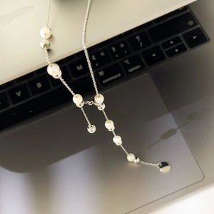 Macro detail of oval chain link necklace with white pearls on a laptop background