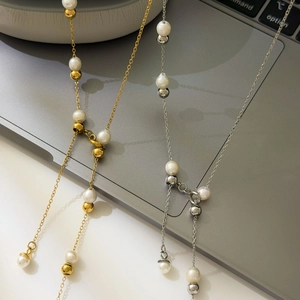Detail of 18K gold and silver plated Y-shaped necklace with white pearl beads on a laptop