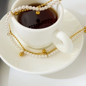 Detail of 18K gold-plated necklace with white pearls and small bells on a coffee cup