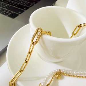 Detailed view of a gold paperclip link necklace with pavé accents and pearl bracelet