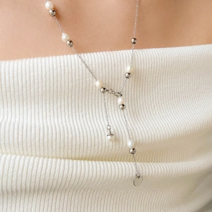 Detail of a silver Y-shaped long necklace with white pearls and polished beads on a model