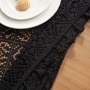 Detail of black crochet hollow tablecloth showing geometric patterns and fringe tassels
