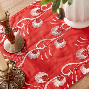 Detail of red table runner with white vine embroidery and red beadwork on wood table