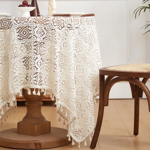 Close-up of beige crochet tablecloth featuring floral hollow patterns and tassel fringe