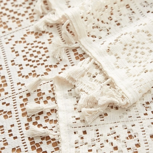 Detailed close-up of beige crochet tablecloth with elegant fringe and floral weave pattern