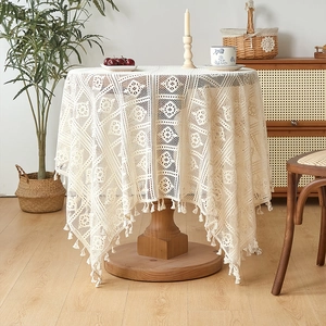 Close-up of beige crochet round tablecloth with delicate tassels and hollow patterns