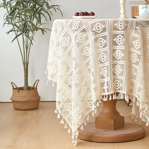 Beige round crochet lace tablecloth with geometric patterns and fringe tassels on wood table