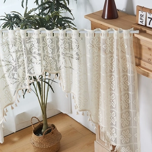 Dettaglio della tenda da caffè in pizzo crema con ricami floreali e nappe decorative