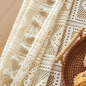Detailed texture of cream crochet table runner with geometric lace and white tassels