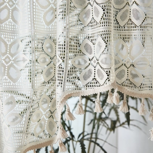 Dettaglio della tenda in pizzo crema con ricami floreali all'uncinetto e nappe decorative